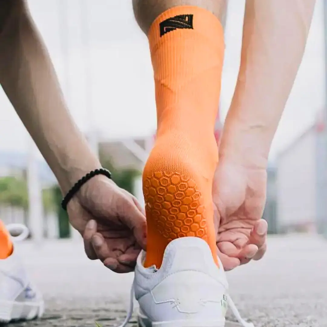 Grip Socken in orangener Farbe. Fußballspieler schlüpft in Fußballschuh.